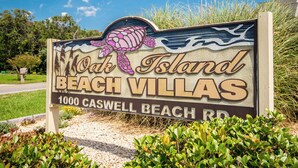 A sign for Oak Island Beach Villas with a turtle graphic and the address 1000 Caswell Beach Rd.