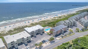 An aerial view of a beachfront hotel with multiple buildings, a swimming pool, and a pier in the background.