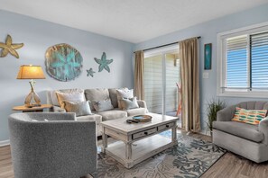A living room with a sofa, armchair, coffee table, and decorative starfish wall art. - Barefeet Retreat: Oceanfront Condo in Caswell Beach (Caswell Beach)