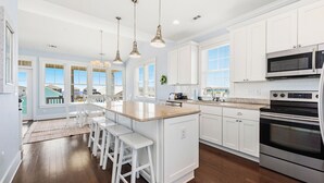 Una cocina moderna con gabinetes blancos, electrodomésticos de acero inoxidable y una isla central con taburetes de bar.