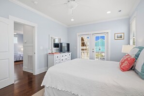 A bedroom with a bed, dresser, TV, and a door leading to another room. - Kiki Hut: Swimming Pool, Great Ocean Views, Dog-Friendly (Oak Island)