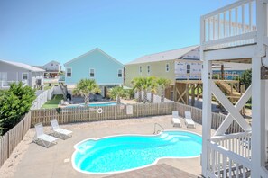 A swimming pool with lounge chairs, a wooden deck, and a fenced area with a view of houses in the background. - Kiki Hut: Swimming Pool, Great Ocean Views, Dog-Friendly (Oak Island)