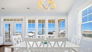 Un comedor con una mesa y sillas blancas, ventanas amplias con vistas y una araña.