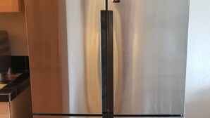 Un réfrigérateur en acier inoxydable doté d’une poignée noire, installé dans une cuisine avec des armoires en bois et un plancher de couleur claire.