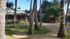 Un complexe hôtelier tropical doté de palmiers, d’une structure à toit de chaume et d’une zone dallée.