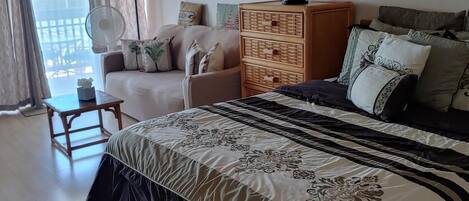 A bedroom with a large bed, a wooden dresser, a sofa, and a fan.