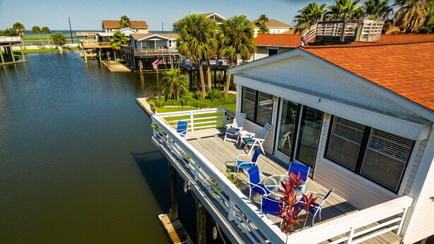 A waterfront house with a deck, outdoor seating, and a view of the water. - Wine Down Large Corner Canal Lot - Sleeps 8 (Jamaica Beach)
