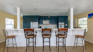 A kitchen with a white island, three bar stools, and dark blue cabinets. - Wine Down Large Corner Canal Lot - Sleeps 8 (Jamaica Beach)