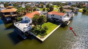 A waterfront property with multiple houses connected by walkways, a dock with a boat, and a small lawn area. - Wine Down Large Corner Canal Lot - Sleeps 8 (Jamaica Beach)