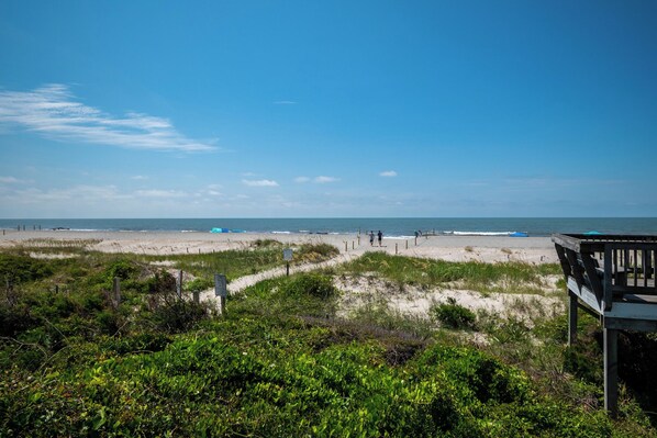 A beach view with a wooden structure, sandy dunes, and a clear sky.