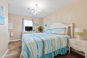Une chambre à coucher comprenant un lit, une table de chevet, une lampe, un téléviseur et une fenêtre avec des stores.