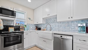 Uma cozinha moderna com eletrodomésticos de aço inoxidável, armários brancos e painel de azulejos azuis.