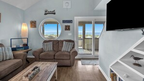Una sala de estar con un sofá marrón, una mesa de centro de madera, un televisor y una estantería.