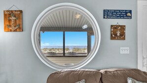 Una habitación con un ventanal redondo grande, una decoración de ancla de madera, un letrero con temática de playa y un adorno de pared de madera.
