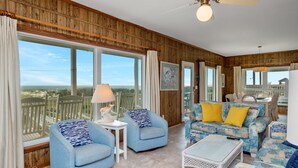 Ein geräumiges Wohnzimmer mit großen Fenstern, einem Deckenventilator und Blick auf den Strand.