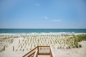 A beach with a wooden walkway leading to the water, grassy dunes, and a clear blue sky.