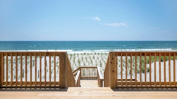 Een houten terras dat naar een strand leidt, met een helder uitzicht op de oceaan.