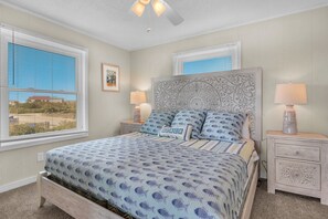Un dormitorio con una cama, dos mesitas de noche, un ventilador de techo y vistas al exterior.