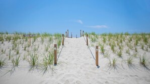 Een zandpad langs het strand dat naar de oceaan leidt, met houten palen en een bord met de tekst 'verboden toegang duinen'.