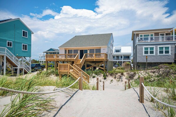 Una propiedad frente a la playa con un sendero arenoso que conduce a una terraza de madera y una escalera.