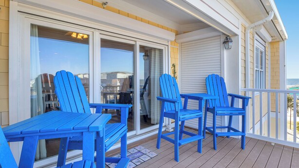 Un espace extérieur abrité, avec des chaises Adirondack bleues et une table, une porte-fenêtre coulissante et une porte de garage blanche.