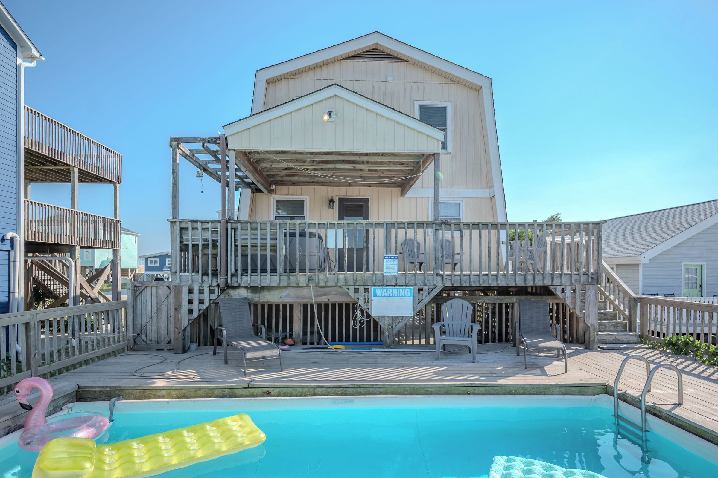 A wooden building with a balcony, a pool with inflatable flamingos, and a warning sign.