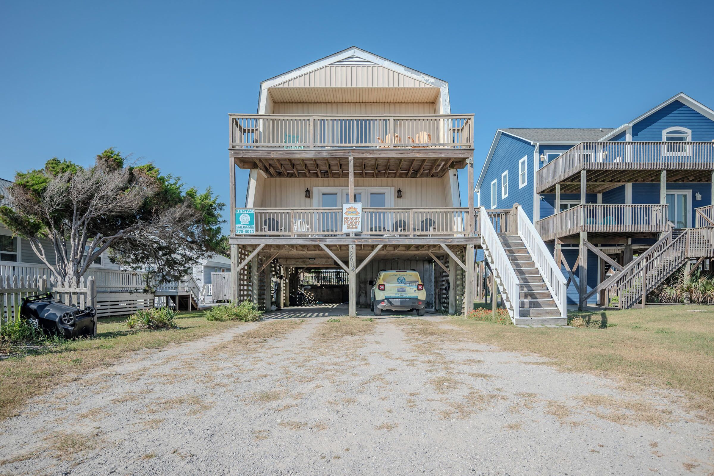 A two-story beach house with a covered driveway and a vehicle parked in front.