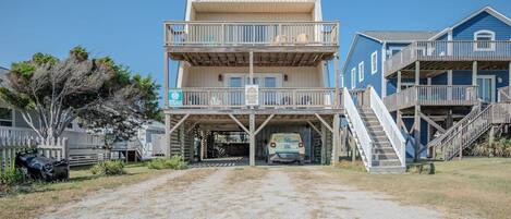 A two-story beach house with a covered driveway and a vehicle parked in front.