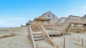 Una casa frente a la playa con un muelle de madera y escaleras que dan a la entrada.