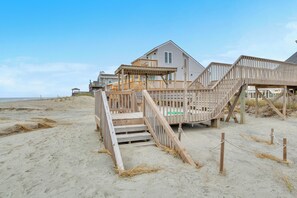 A beachfront house with a wooden deck and stairs leading to the entrance.