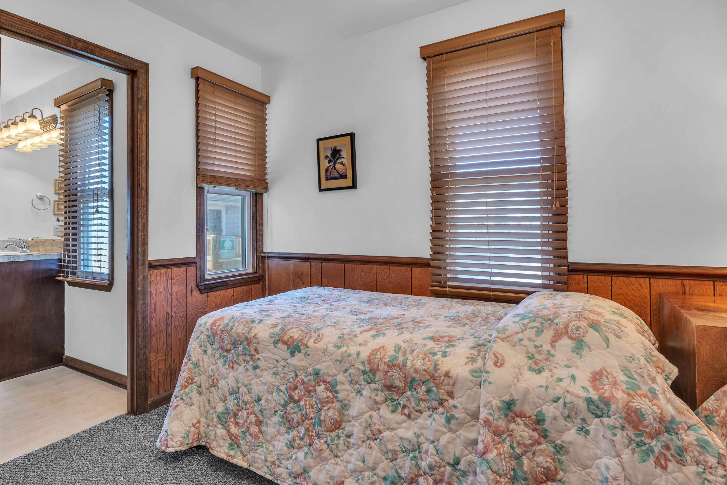 A bedroom with a floral bedspread, wooden headboard, and a large mirror.