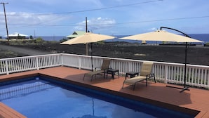 Une piscine avec une terrasse en bois, deux chaises beiges et une clôture blanche.