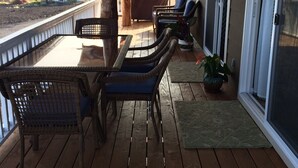 Un espace extérieur abrité, doté d'un plancher en bois, de meubles en osier et offrant une vue sur des bâtiments éloignés.