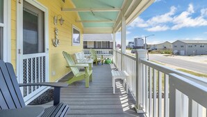 En veranda med grønne Adirondack-stole og en bænk, et hvidt gelænder og frit udsyn til gaden og andre bygninger i baggrunden.