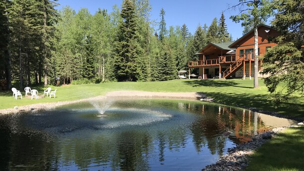 A lodge with a pond, surrounded by trees, and a deck with chairs. - "Serene, tranquil home near Glacier National Park, great for 2 Families!" (Columbia Falls)