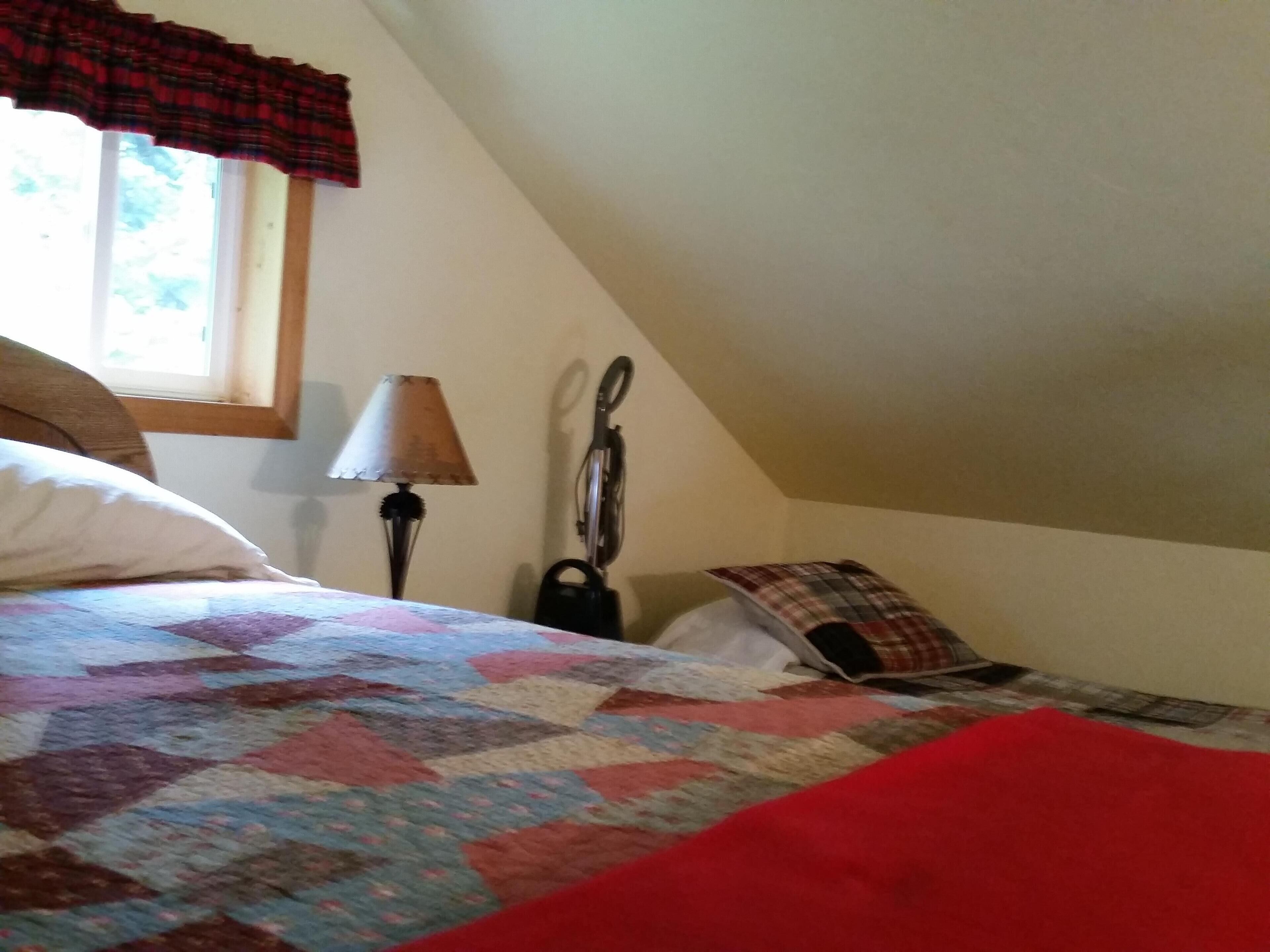 Een slaapkamer met een bed, een raam met gordijnen in ruitpatroon, een lamp en een fiets.