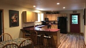A compact kitchen with wooden cabinets, a dining area with a table and chairs, and a refrigerator. - "Serene, tranquil home near Glacier National Park, great for 2 Families!" (Columbia Falls)