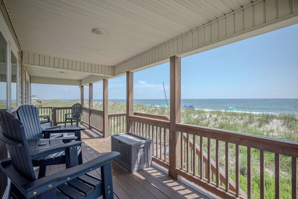 A covered deck with wooden railings, two Adirondack chairs, and a small table.