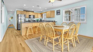 A modern kitchen with wooden cabinets, a central island, and a dining area with wooden chairs.