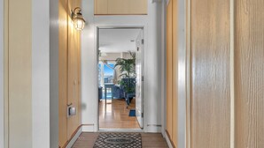 A hallway with a wooden door, a welcome mat, and a light fixture. - Beats Working: Condo with Community Pool Near OKI Pier and Restaurants (Oak Island)