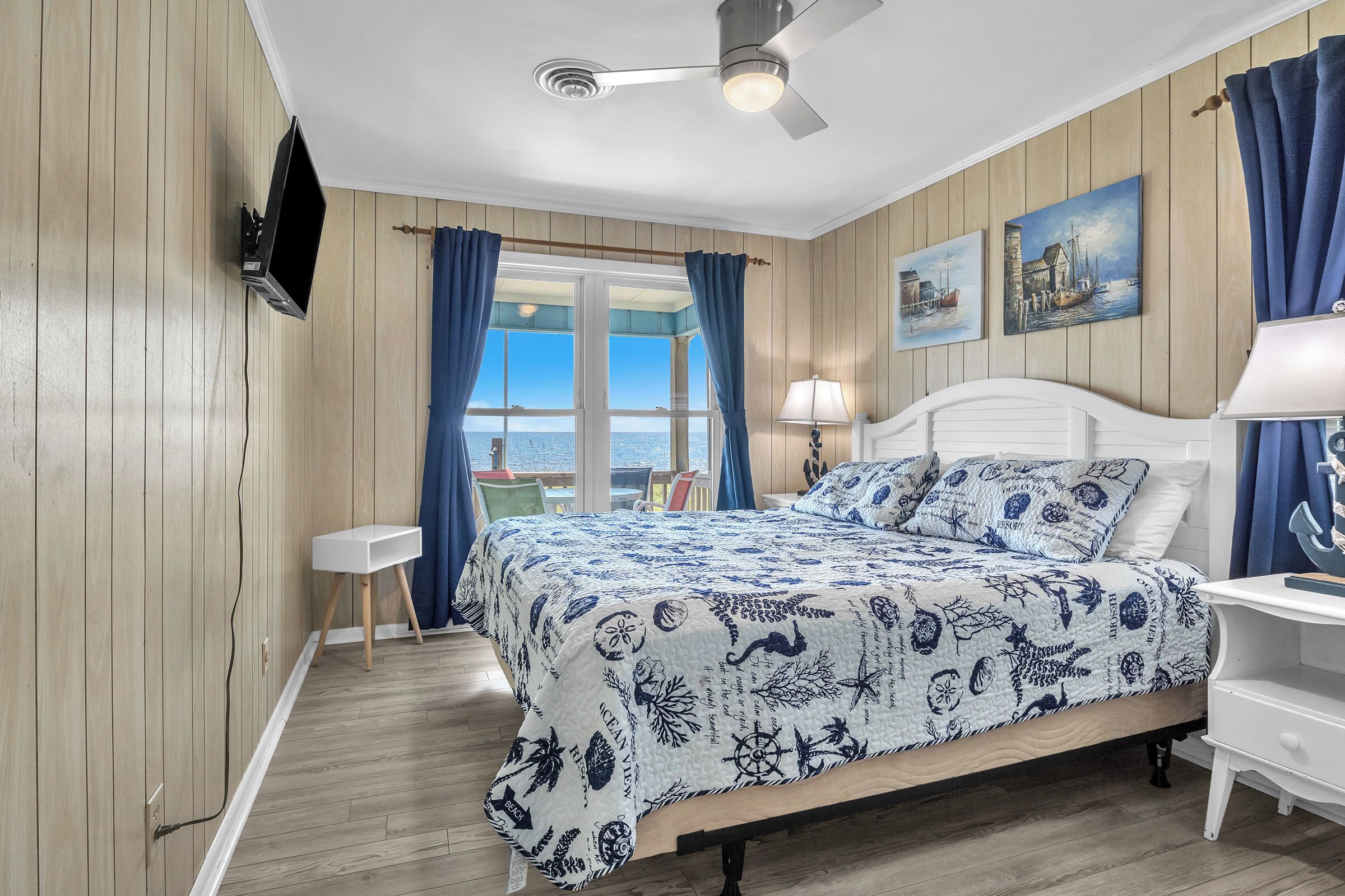 Une chambre à coucher comprenant un lit, un bureau, une chaise, un téléviseur fixé au mur et une fenêtre avec des rideaux.