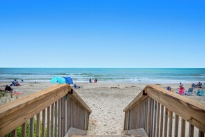 Una terraza de madera que da a una playa, con una tienda de campaña y sillas de playa.