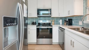 Eine moderne Küche mit Edelstahlgeräten, weißen Schränken und einer blau gefliesten Spritzschutzwand.