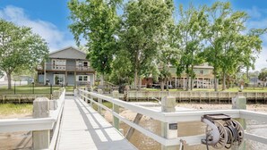 A wooden boardwalk leading to a building with a balcony, surrounded by trees and a fenced area.