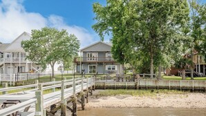 A waterfront property with a wooden pier, a sandy beach, and a house with a balcony.