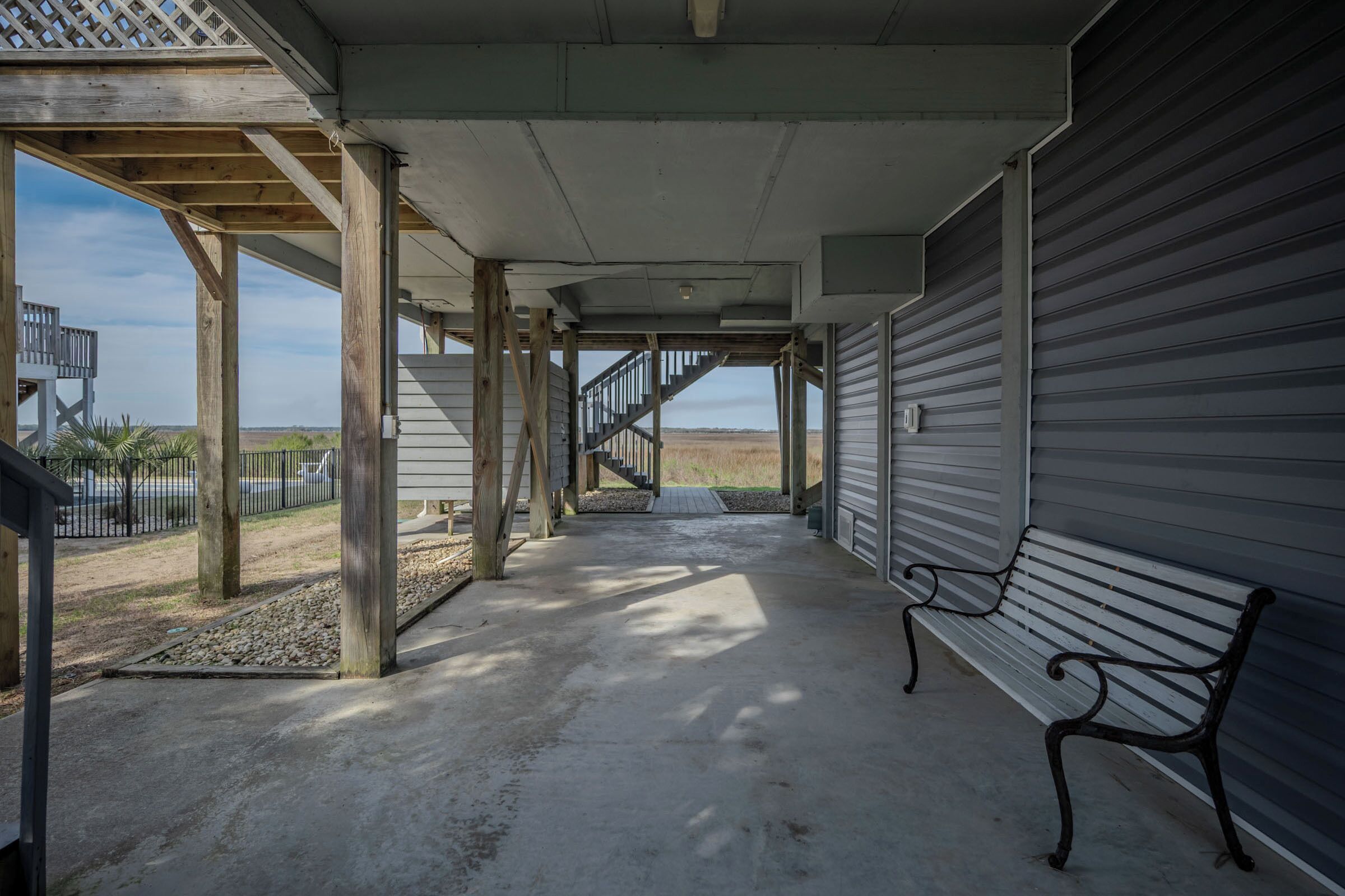 A covered outdoor area with a bench, wooden columns, and a view of the beach.