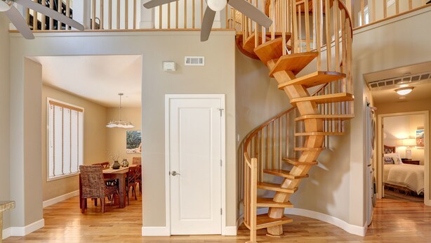 A spacious living area with a wooden staircase, a dining area with wicker furniture, and a view of the adjacent bedroom. - Bikini Bungalow - Large condo, Steps from Beach + Parking, Family (Avila Beach)