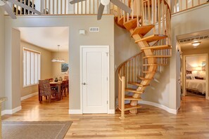 A spacious living area with a wooden staircase, a dining area with wicker furniture, and a view of the adjacent bedroom. - Bikini Bungalow - Large condo, Steps from Beach + Parking, Family (Avila Beach)