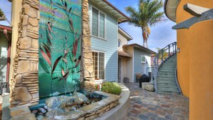 A stone fountain with a water feature, a curved stone wall, and a staircase leading to a door. - Bikini Bungalow - Large condo, Steps from Beach + Parking, Family (Avila Beach)