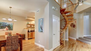 A spacious living area with a wooden staircase, a dining table with chairs, and a kitchen in the background. - Bikini Bungalow - Large condo, Steps from Beach + Parking, Family (Avila Beach)